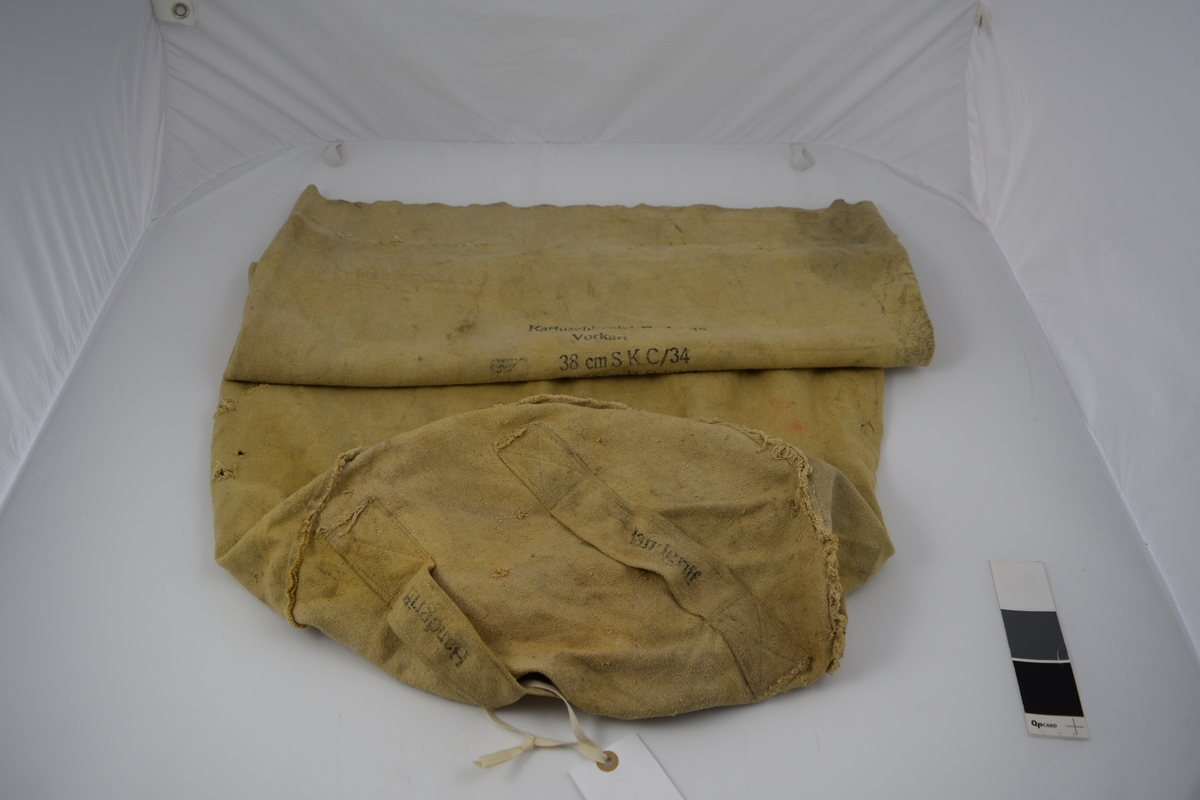 Original karduspose for drivladning tilhørende til 38 cm SK C/34 kanon på Møvig Fort. Sylindrisk form av et stykke med påsydd rundt bunn. To påsydde handtak. Håndsydde sting langs toppen.