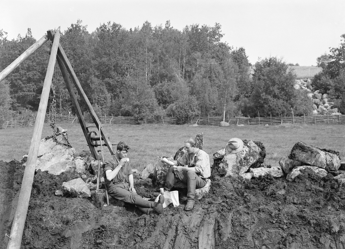 Gunnar och Emil Hultgren har tagit kafferast från dikesgrävning. Med hjälp av stubbrytaren och spade gör de några gärden i Bona mindre vattensjuka. Året är 1929.
Den skarpögde kan ana de ritsar som markerar var fotograf Hultgren tänkte sig beskära bilden.