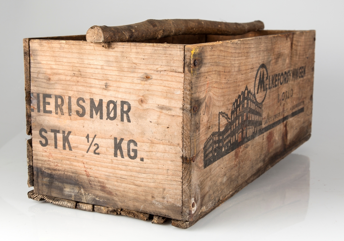 Trekasse fra Meieriforsyningen til transport og oppbevaring av smørpakker. Uoriginalt, enkelt håndtak av trepinne med bark.