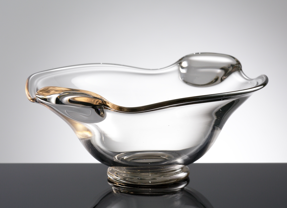 Skål. 
Formgiven av Hugo Gehlin.
Beskrivning: Närmast oval (oregelbundet). Foten rund. Två handtag av tjockare glas. Avrundat mot botten, utsvängd i överdelen.
Färg: Ofärgat klarglas.
Mått: Ovan anges största höjd, bredd, längd samt fotens diameter.
Inskrivet i huvudkatalogen 1955.

Funktion: Skål