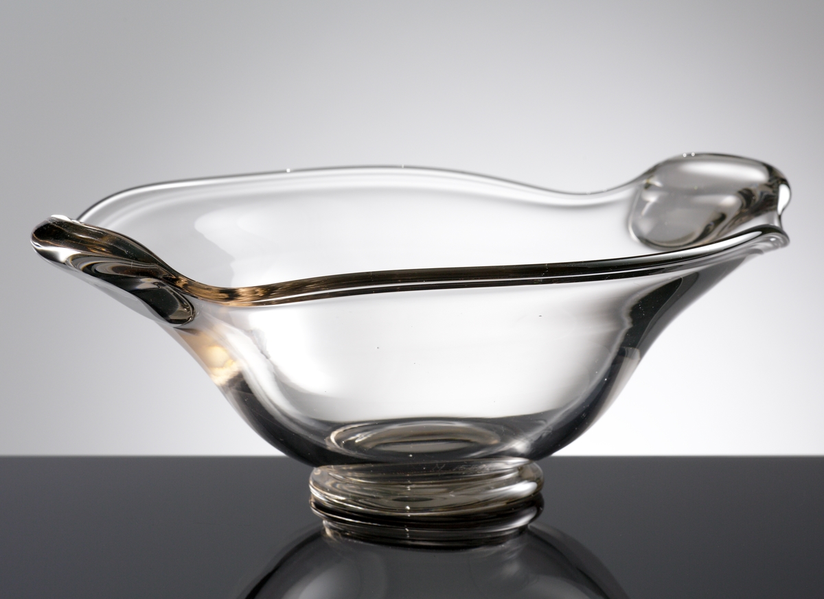 Skål. 
Formgiven av Hugo Gehlin.
Beskrivning: Närmast oval (oregelbundet). Foten rund. Två handtag av tjockare glas. Avrundat mot botten, utsvängd i överdelen.
Färg: Ofärgat klarglas.
Mått: Ovan anges största höjd, bredd, längd samt fotens diameter.
Inskrivet i huvudkatalogen 1955.

Funktion: Skål