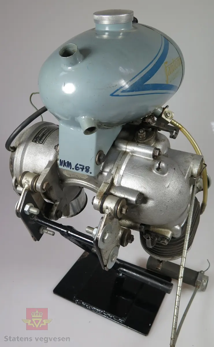 Fantom Bj.52. 48 ccm forbrenningsmotor med tank og lys. Er her montert på et stativ. Er lagd for å kunne monteres foran på sykkel slik at gummi hjulet på denne motoren skal dra rundt hjulet på sykkelen. Motoren har 1,4 hk og er av typen 4-takt, den går på ren bensin.