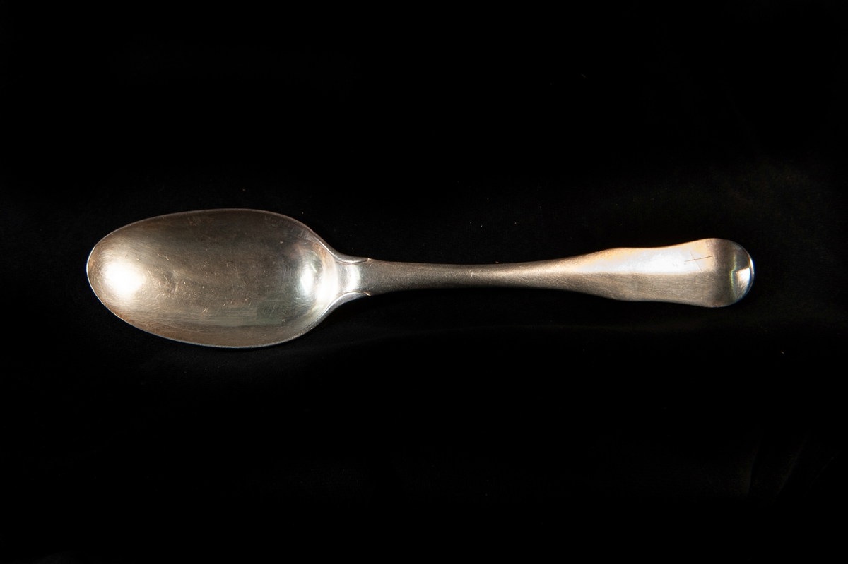 En matsked av silver. Enkel s.k. fiolmodell med antydantill ås. Stämplad på skaftets baksida.

Jfr JM 18809.