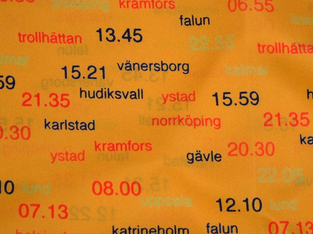 Gul scarf, med stationsnamn och tider i röd och blå text.