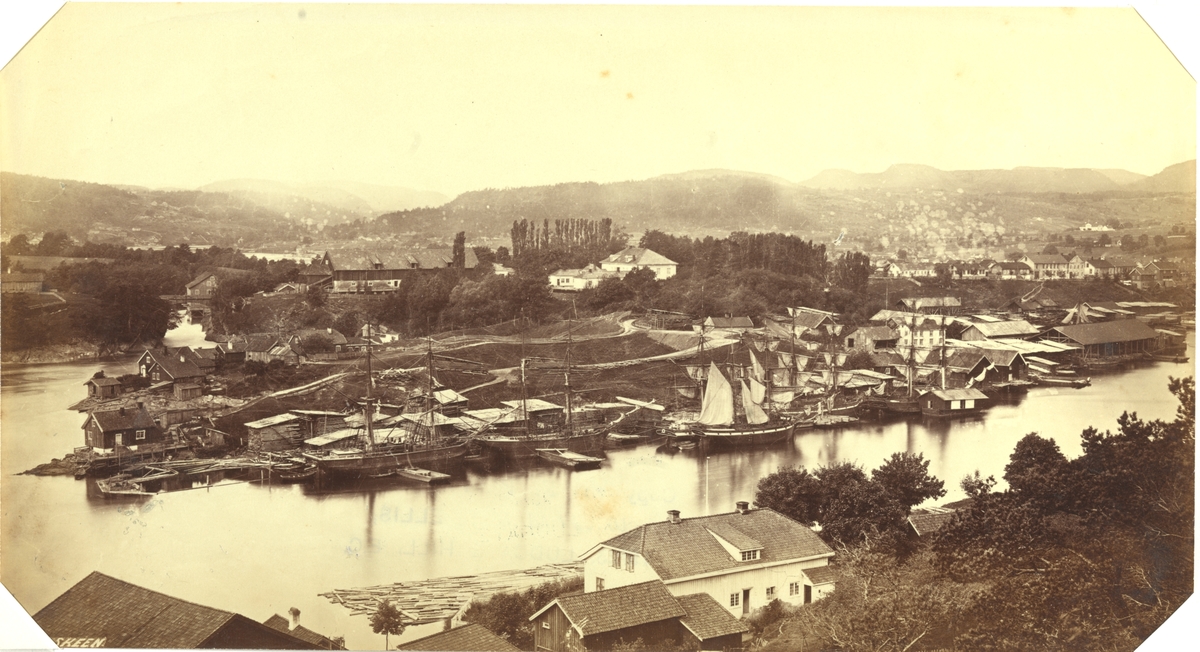 Havneanlegg i Skien med seilskip ved kaien. Spredt bebyggelse i forgrunn og bakgrunn. Fotografert mellom 1870 og 1886.