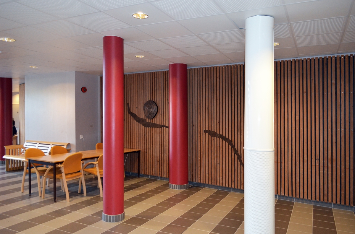 Kunstverket består av bronseelementer som er felt inn i veggen i to etasjer. Motivene er avstøpninger av bølgepapp og sandblåste tverrsnitt av trestammer.  Arbeidet inngår i en utsmykning som omfatter to deler, en utendørs og en innendørs.