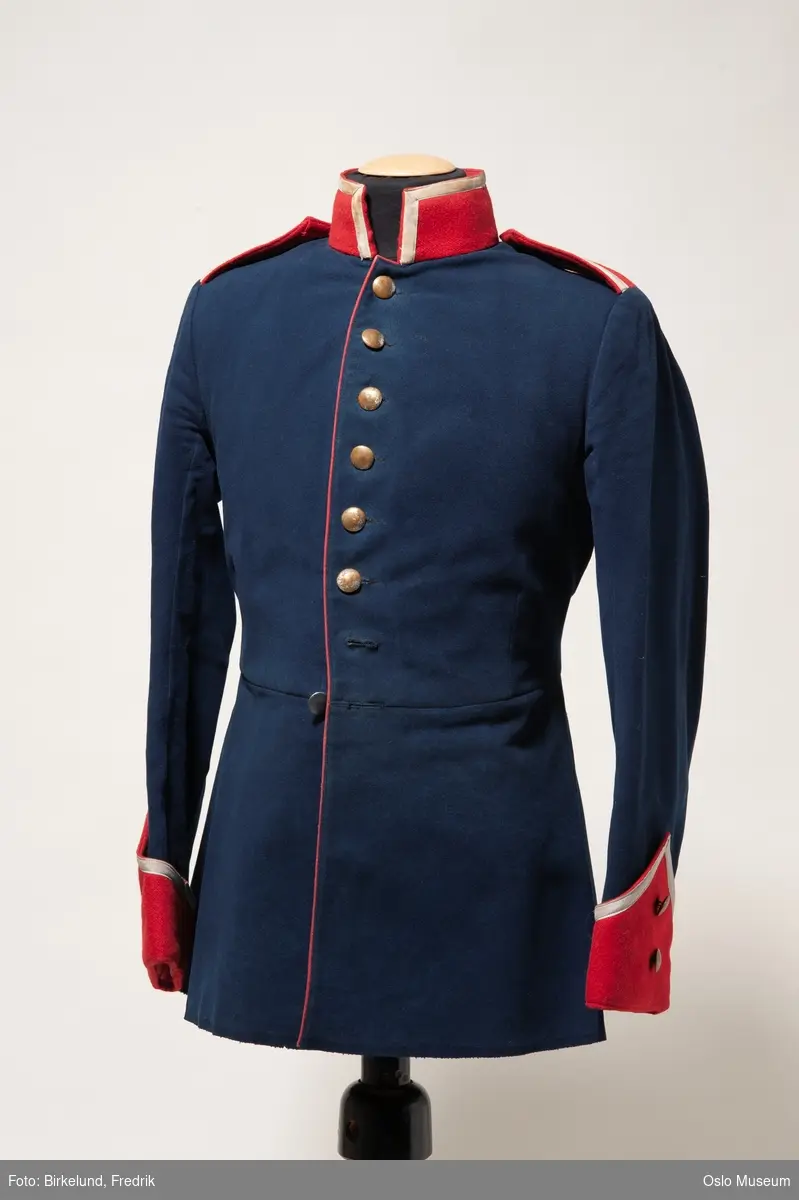 A: uniformsjakke, blå ull med røde mansjetter og rød, høy krave. Lukkes med metallknapper i front.
B: uniformsjakke, blå ull med røde mansjetter og rød, høy krave. Lukkes med metallknapper i front.