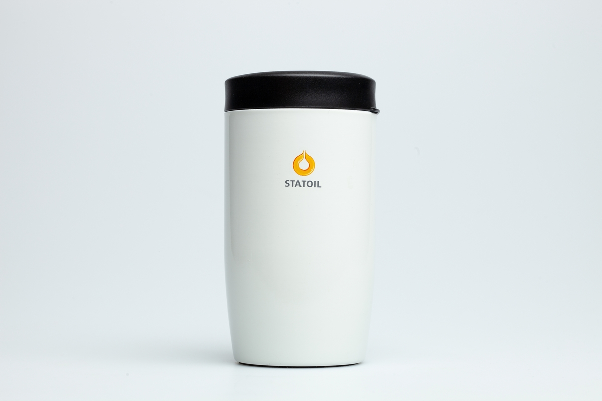 En hvit Statoilkopp med sort hank. Koppen er i grå metall på innsiden. Statoillogo i oransje på koppen. På en etikett på koppen er en Statoillogo,