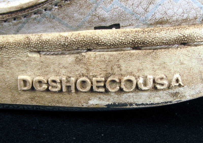 a) skateboardbräda av trä. Hjul saknas. Mått: längd 77,5 cm, bredd 19 cm, tjocklek 1 cm.
b1-b2) svarta skateskor. Märke: DC Shoe.
Märkning: "DCSHOECOUSA".
 Mått: längd 23 cm, bredd 9 cm, höjd 8,5 cm.
c1-c2) vita skateskor.  Märke: DC Shoe. 
Märkning: "DCSHOECOUSA". 
Mått: längd 22 cm, bredd 8, 5 cm, höjd 8,5 cm.