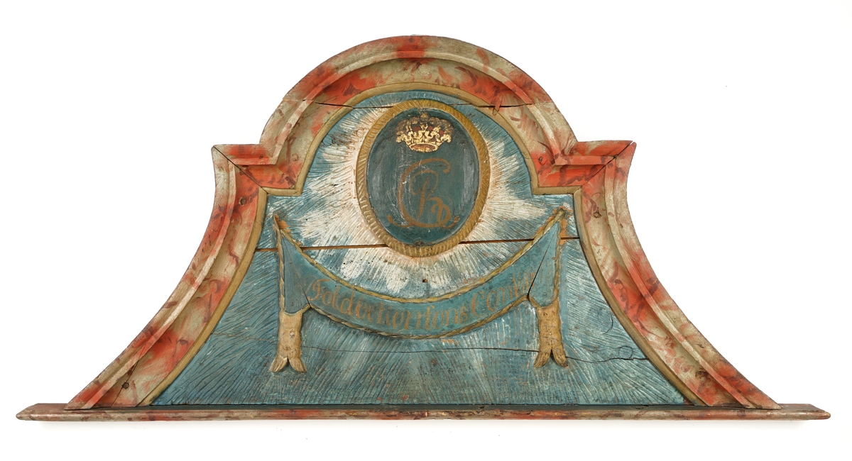 Døroverstykke bestående av 3 sammensatte trebord med not og fjær (bunnplaten). Trekantet med rett underkant, innadbuede sider og utadbuet overkant. Bunnplaten er utskåret og i flere nyanser av blått ,påsatt 2 forhøyninger. Den øverste er oval, blå med krone i gull og rødt over "CR" i brunt, langs kanten en lysutskåret bord. Den nederste er avlang, buet, blå med "Toldbetientens Contoir" skrevet med brunfarge. Langs kanten en lysutskåret bord, på hver side en lys,utskåret dusk. Skiltet omgitt av en rett list i underkant, en rød og grå buet,profilert list på sidene og i overkant.Tilhører et sett med tre døroverstykker .Jfr. B-bok nr. 518,519,520. Nr. 518 er borte (ToldCassererens Contoir") Antatt fra Christiania jfr. B-bok.