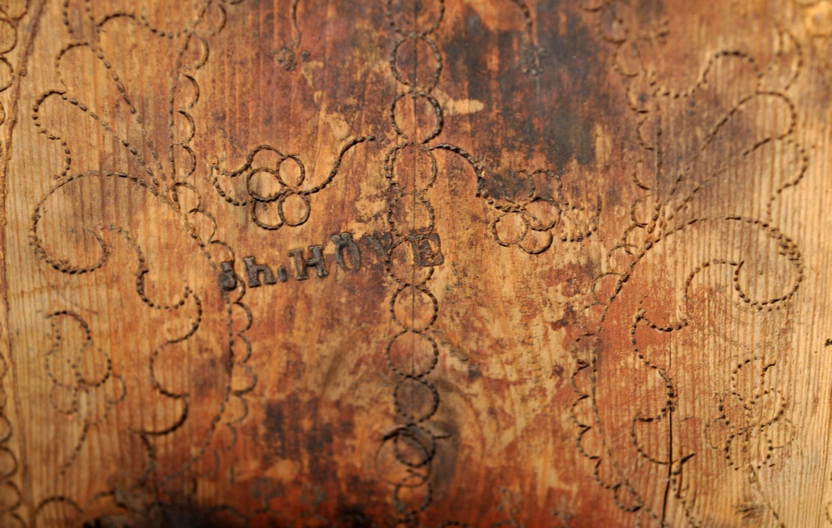 Sveipet laup med rett bakstykke, lagd for å kunne henges på en vegg, der den skulle henge som en beholder, opprinnelig sannsynligvis på et kjøkken. Sett rett ovenfra eller nedenfra er laupen formet som en halvoval. De veggene som skulle vende fram i rommet er lagd av tre forholdsvis tynne (7-8 millimeter) bjørkeskier, som er bøyd i en U-form. Endestykkene er festet i slisser langs kantene av bakstykket ved hjelp av trenagler. Disse tre komponentene er bundet sammen, kant mot kant ved hjelp av bindsler av trefibermateriale. Ytterflatene har svidekor - bølgemønstere på den øverste og nederste, og en akantusranke på den midtre, som er noe bredere enn de to andre. Bakstykket - ryggfjøla - er lagd av et 21,3 centimeter bredt og 1,9 centimeter tjukt (3/4-toms) bord, antakelig av granvirke. Det er vinkelrett avkuttet i den nedre enden, men overenden er avrundet og profilert. Her er det fire gjennbombrutte hull, hvorav tre er runde og det fjerde er firefliket. Det øverste av disse har vært brukt ved oppheng. Også denne delen av laupen har svidekor med elementer av de samme formene som finnes på veggenes forsider. På baksida er det innsvidd en ring, sammensatt av små sirkler, som omgir initialer og årstall: «KSS 1817». Forsida er svijernstemplet «Jh. HØYE». Laupen har et halvovalformet lokk, lagd av granvirke og prydet med et innsvidd mønster, bestående av sirkler, halvsirkler og akantusblader. Også her finner vi det nevnte svijernstempelet. Lokket og bakstykket kan se ut til å ha vært innsatt med et rødbrunt fargestoff. Opprinnelig hengsling mangler. Botnstykket mangler fullstendig, men et innfelt spor nederst på bakstykket og naglehull langs ytterkanten på den nederste buete skia antyder hvordan botnstykket har vært festet.