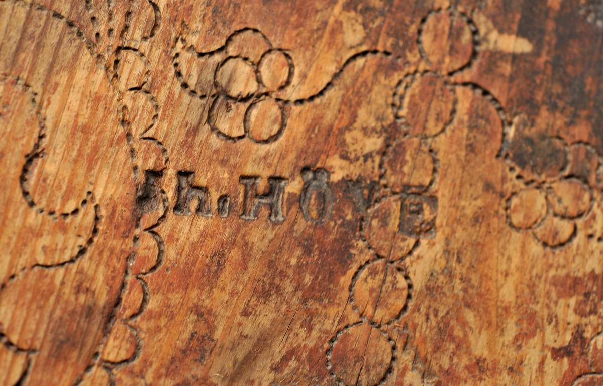 Sveipet laup med rett bakstykke, lagd for å kunne henges på en vegg, der den skulle henge som en beholder, opprinnelig sannsynligvis på et kjøkken. Sett rett ovenfra eller nedenfra er laupen formet som en halvoval. De veggene som skulle vende fram i rommet er lagd av tre forholdsvis tynne (7-8 millimeter) bjørkeskier, som er bøyd i en U-form. Endestykkene er festet i slisser langs kantene av bakstykket ved hjelp av trenagler. Disse tre komponentene er bundet sammen, kant mot kant ved hjelp av bindsler av trefibermateriale. Ytterflatene har svidekor - bølgemønstere på den øverste og nederste, og en akantusranke på den midtre, som er noe bredere enn de to andre. Bakstykket - ryggfjøla - er lagd av et 21,3 centimeter bredt og 1,9 centimeter tjukt (3/4-toms) bord, antakelig av granvirke. Det er vinkelrett avkuttet i den nedre enden, men overenden er avrundet og profilert. Her er det fire gjennbombrutte hull, hvorav tre er runde og det fjerde er firefliket. Det øverste av disse har vært brukt ved oppheng. Også denne delen av laupen har svidekor med elementer av de samme formene som finnes på veggenes forsider. På baksida er det innsvidd en ring, sammensatt av små sirkler, som omgir initialer og årstall: «KSS 1817». Forsida er svijernstemplet «Jh. HØYE». Laupen har et halvovalformet lokk, lagd av granvirke og prydet med et innsvidd mønster, bestående av sirkler, halvsirkler og akantusblader. Også her finner vi det nevnte svijernstempelet. Lokket og bakstykket kan se ut til å ha vært innsatt med et rødbrunt fargestoff. Opprinnelig hengsling mangler. Botnstykket mangler fullstendig, men et innfelt spor nederst på bakstykket og naglehull langs ytterkanten på den nederste buete skia antyder hvordan botnstykket har vært festet.