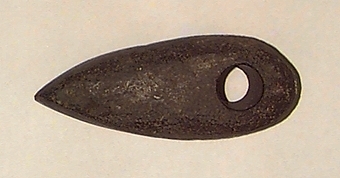 Skafthålsyxa av bergart. Skafthålet placerat långt bakåt. Välvd ovansida, plan undersida. Rundad nacke.