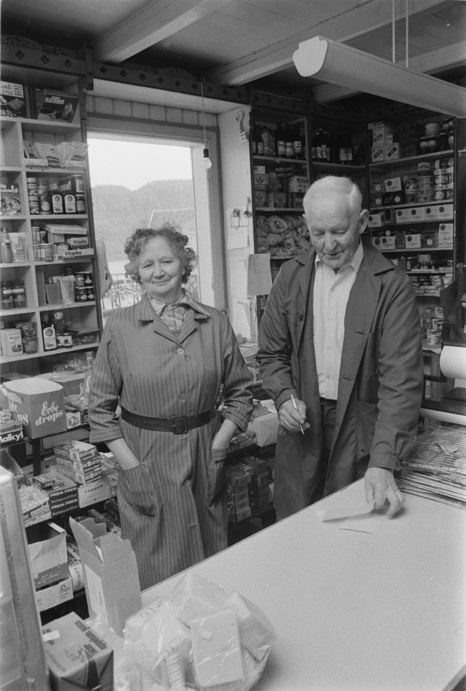 Leirfjord, Nedre-Leland. Johan Bergh og kona Aslaug Bergh, eiere av Berghs landhandel (butikk), bak disken med noe av vareutvalget i butikken. Butikken er nå museum.
Bildet fra Helgeland Arbeiderblad sin sommerpatrulje.
Finnes også som VBH.F.2011-010-0003