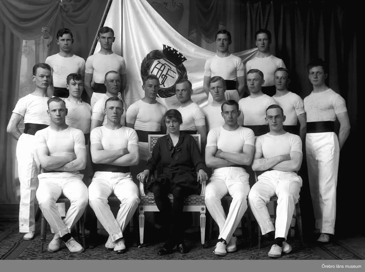 Interiör, grupp 18 personer, Arbetarnas Gymnastikförening (AGF).
 Ledare Greta Adrian.
Till vänster om Greta Adrian sitter Nils Ström "Stans vigaste klump".
