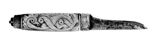 Tollekniv med slire.  Knivens lengde er 20 centimeter.  Den har et gulkvitt beinskaft, som er 10,7 centimeter langt og har et noe konvekst lengdesnitt og et noenlunde ovalt tverrsnitt.  Midten av skaftet måler 2,7 X 2,1 centimeter.  Overflata er prydet med et akantusrelieff.  Langs skaftryggen er det et glatt felt med initialer og årstall: «N P S F[?] 1887».  Det er nærliggende å anta at dette må ha vært en tidligere eiers initialer og anskaffelsesåret.  Beinskaftet har hatt messingholker i begge ender, men bare framholken (nærmest bladet) var intakt da kniven kom til museet.  Den er 1,1 centimeter bred og prydet med linjer langs ytterkantene, ellers glatt.  I overenden av skaftet later det til at ytterspissen på bladtangen er gjenget og påskudd ei kvadratisk mutter med skrådde sideflater.  Bladet er 8,6 centimeter langt og 2,3 centimeter bredt ved brystningen.  Videre framover er imidlertid bladet betraktelig smalere, på grunn av gjentatt sliping.  Den bakre delen av knives nakkeparti er 0,5 centimeter tjukk.

Slira er utført i lær med holker av messing og vedhengslet stropp for knappefeste i bukselinninga.  Samlet lengde er 27,8 centimeter.  Sjølve slira er 16 centimeter lang, fra enden av doppskoen til overkanten av munningsholken (målt på framsida, ikke hengslingspunktet bak).  Slirelæret er mørkebrunt og sammensydd med en søm som er plassert på «baksida», altså den sida som skulle vende inn mot bærerens kropp.  Framsida av doppskoen er merket med årstallet «1851», altså en datering som overgår den vi finner på knivskaftet med 36 år.  På baksida av doppskoen er det inngravert et symmetrisk akantusmønster med C-ornamenter.  Doppskoen er naglet fast i slirelæret ved hjelp av ei gjennombrutt nagle.  Akantusmønsteret fra doppskoens bakside finne vi igjen også på midtholken, som er drøyt 1,8 centimeter bred.  Ettersom holkene ikke er forbundet ved hjelp av sideskinner er også midtholken forankret i læret ved hjelp av nagler på sliras bakside.  Overholken eller munningsholken er 1,9 centimeter bred, og har samme akantusmønster som midtholken og baksida av doppskoen.  Også her er det naglefester i slirelæret.  Munningsholken har en sprekkskade, egentlig et brudd, på det som framstår som baksida av slira.  Her finner vi også et hengslingspunkt med ei U-formet bøyle som danner overgang til ei 4,5 centimeter lang og 1,5 centimeter bred messingspenne.  På forsida av denne spenna er det akantusdekor, på baksida finner vi initialene «B C L».  Spenna må ha vært beregnet på feste av knivslira i linninga på bærerens bukse.  Da kniven ble overlatt til museet var den imidlertid utstyrt med ei lærhempe med en splitt som kunne tjene som festepunkt på en knapp.