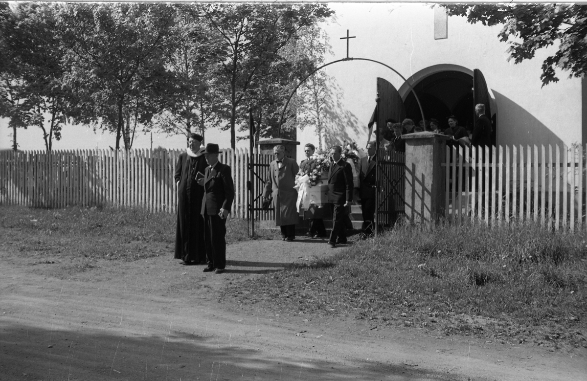 Begravelse ved Hoff kirke juni 1955. Serie på 9 bilder, der de første viser prosesjonen fra gravkapellet il grava, de øvrige ved grava. Ifølge informmant er dette begravelsen etter Ludvig Madshus som var kjøpmann i Lillo. Foraan prosesjonen går presten, som trolig er Finn Sommer, og kirketjener Pål Rødset. Nærmest bak kista trolig Ludvigs hustru Helga født Hagen, og deres to sønner Johan Ludvig (i midten) og Olav. De øvrige er ukjente.