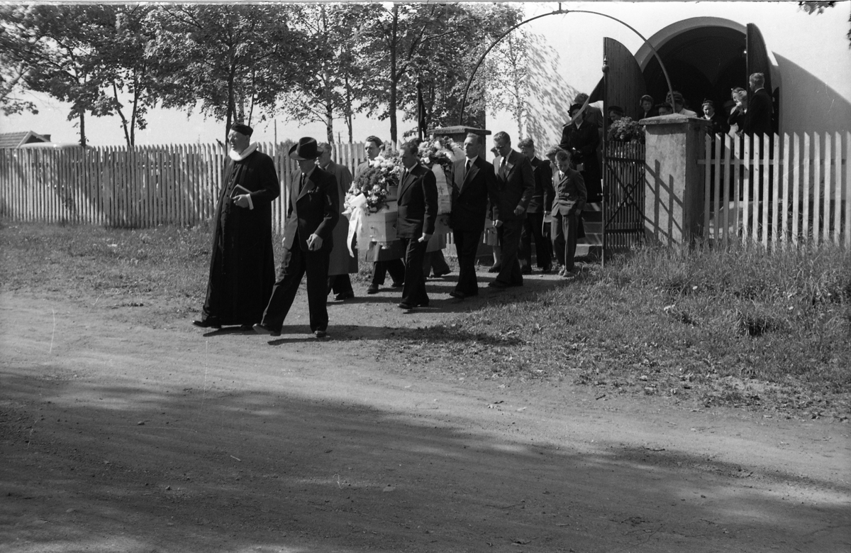 Begravelse ved Hoff kirke juni 1955. Serie på 9 bilder, der de første viser prosesjonen fra gravkapellet il grava, de øvrige ved grava. Ifølge informmant er dette begravelsen etter Ludvig Madshus som var kjøpmann i Lillo. Foraan prosesjonen går presten, som trolig er Finn Sommer, og kirketjener Pål Rødset. Nærmest bak kista trolig Ludvigs hustru Helga født Hagen, og deres to sønner Johan Ludvig (i midten) og Olav. De øvrige er ukjente.