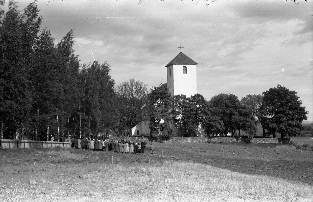 Begravelse ved Hoff kirke juni 1955. Serie på 9 bilder, der de første viser prosesjonen fra gravkapellet il grava, de øvrige ved grava. Ifølge informmant er dette begravelsen etter Ludvig Madshus som var kjøpmann i Lillo. Foraan prosesjonen går presten, som trolig er Finn Sommer, og kirketjener Pål Rødset. Nærmest bak kista trolig Ludvigs hustru Helga født Hagen, og deres to sønner Johan Ludvig (i midten) og Olav. De øvrige er ukjente.