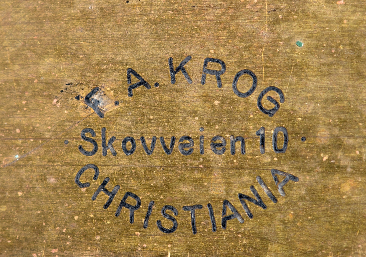 Kubikkberegningsapparat, levert av produsenten F. A. Krog i Skovveien i Kristiania, antakelig tidlig på 1900-tallet.  Apparatet er formet som et rektangulært skrin, utført i eiketre, men med "lokk" av ei messingplate.  Langs midtaksen på dette lokket er det ei lang, smal, rektanuglær spalte med glass under.  Gjennom denne ser vi ned på en tabell.  Tabellen er trykket på en papirrull, som er forankret på to valser nede i skrinet.  Tabellen kan beveges ved hjelp av dreiehjul på skrinets endeflater, to på hver side, ett i hver ende av de nevnte valsene.  Lengst til høyre i tabellvinduet finner vi "klassifiseringsinformasjon" - angivelser av stokklengder, diametere og salgsklasser.  Langs den øvrige delen av vinduet kan man lese av kubikkmeterangivelser for fra 1 til 70 stokker med samme dimensjoner og klassespesifikasjon.  Avlesinga skjer fra en tolinjet tabell på den nevnte papirrullen inne i skrinet, og med stokketallesangivelser på lokket - 1-35 stokker på oversida av vinduet og 36-70 stokker på undersida.  Det nevnte emaljerte lokket, som er hvitt med svarte tall og bokstaver, er skrudd fast til toppen av skrinet.  Det er grunn til å tro at valsene med tabellen må være montert før dette ble påsatt.  Skrinet er ellers lagd av høvlet eiketre, og den holdes sammen av de nevnte skruene i lokket og spiker fra botnstykket.  På standflata er det også hengslet en klaff, som kan vippes opp, slik at lokket skrår mot brukeren når apparatet brukes på et bord eller et annet plant underlag. 