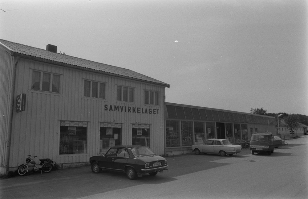 Leirfjord, Leland. Samvirkelaget (det "gamle" samvirkelaget) med biler og moped parkert på utsiden.
Bildet fra Helgeland Arbeiderblad sin sommerpatrulje.
Finnes også som VBH.F.2011-010-0080