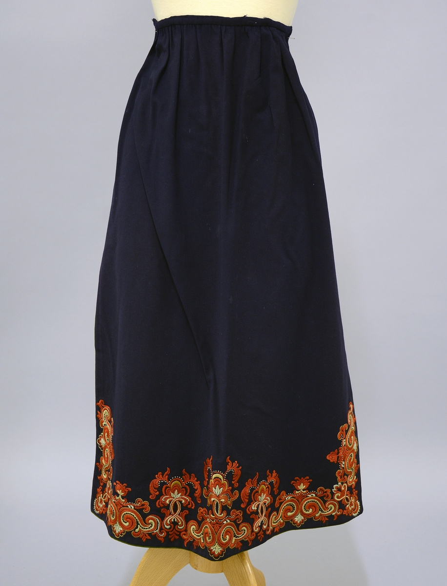 Øst-Telemarksbunad, sydd av Anne Bamle i 1926.TGM-BM.1977:381.A-E 
D. Forkle. Bredde 66 cm nede, opp er det rynket sammen til 34 cm og sydd til en 34 cm lang og 1 cm bred linning, som er tråklet først i stakken. 4 cm nedenfor baugen, slik at brikkebåndet dekker over det. Forkleet er på 3 sider kantet med grønt som stakken nede. Broderiene er dekket av atlas fòr på vrangen. Rosesaum 20cm høy på sidene. 16 cm høy på midten, bygget på samme motiv som stakken. Fra Protokoll.