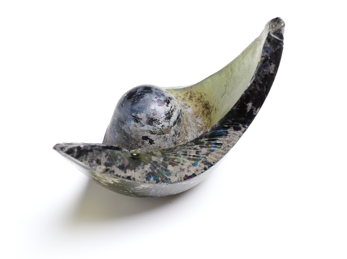 Fragment av buteljgrönt glas. Del av den smalare bottnen av rund flaska med massiv upphöjning i bottnens mitt.