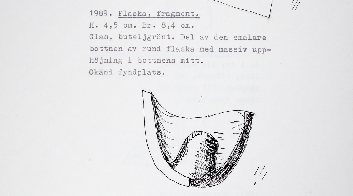 Fragment av buteljgrönt glas. Del av den smalare bottnen av rund flaska med massiv upphöjning i bottnens mitt.