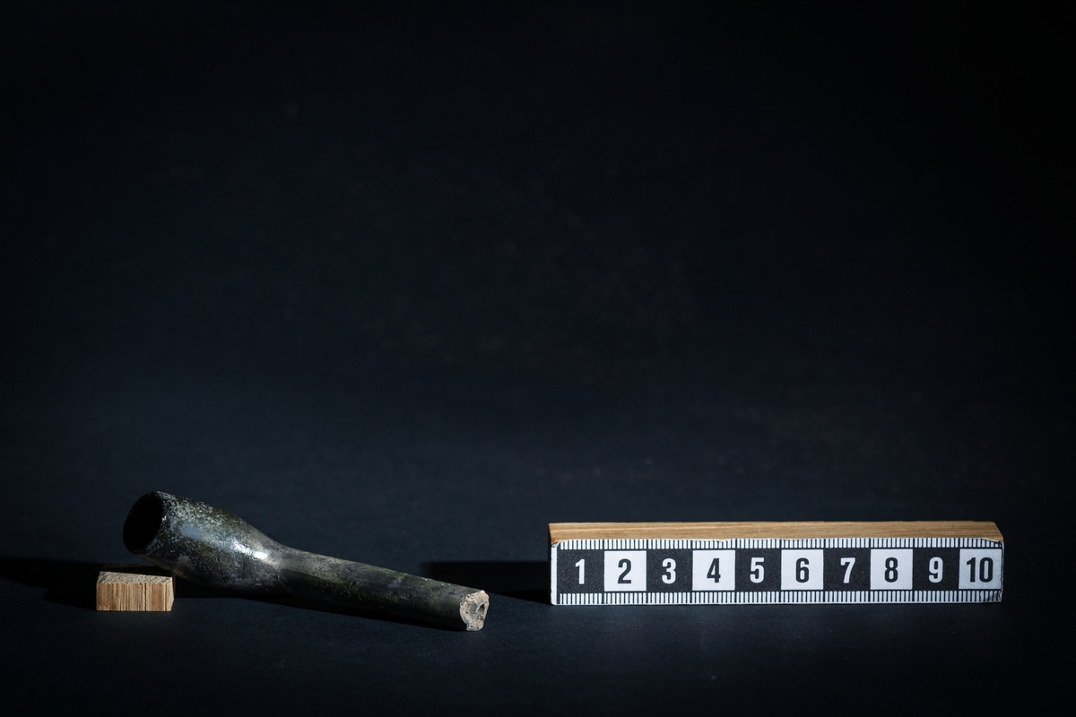 Brungrå kritpipa. Avbrutet skaft. Relativt stor klack på undersidan innan skaftet svänger till huvud och kammare.