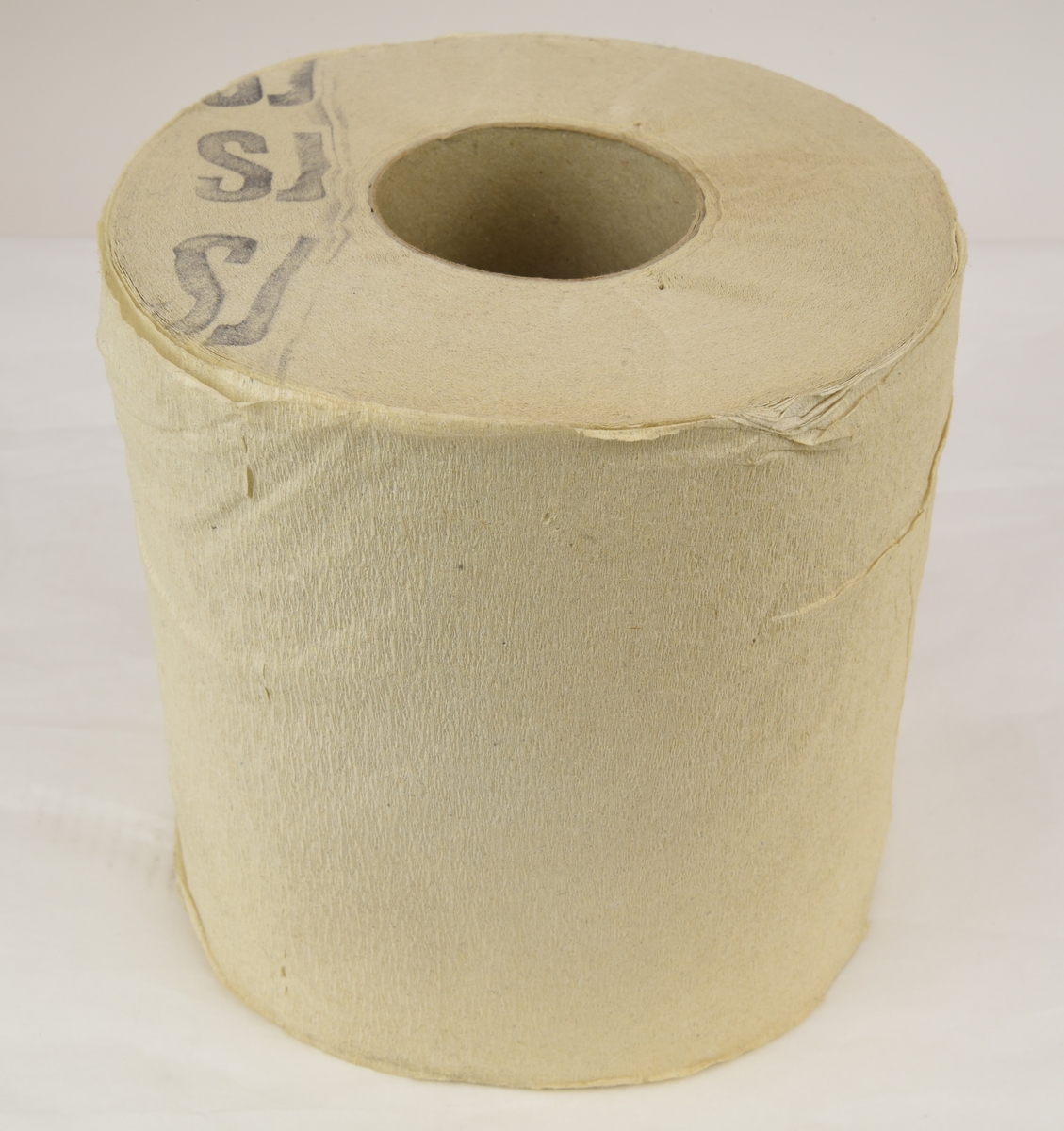 Toalettpappersrulle av svagt kräppat papper. Rullen är stämplad SJ på ena sidan med en mörk färg.