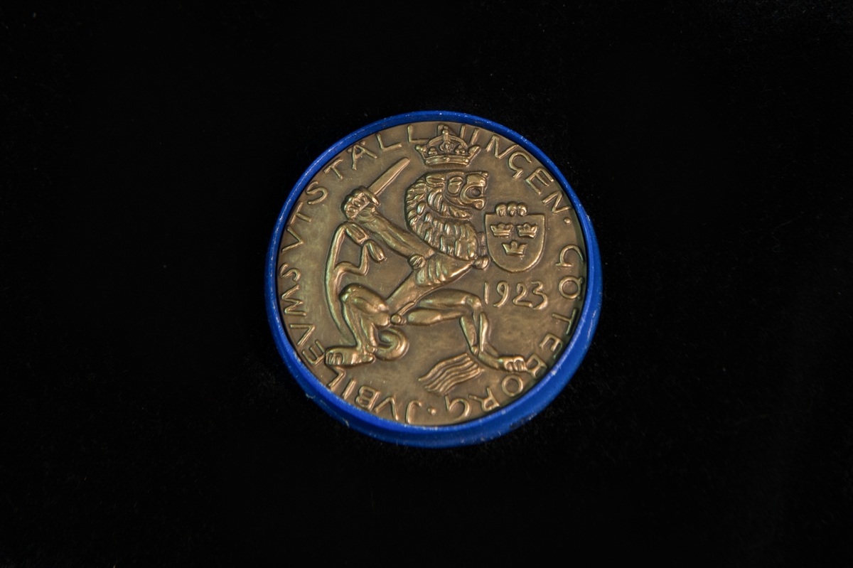 Utställningsmedalj av metall, förvarad i rund pappask klädd i blå papp med guldigt tryck på locket, "C.C. Sporrong  Co, kungsgatan 17, Stockholm". Även botten är tryckt med samma text i svart på beige botten.

Medaljens åtsida präglad med 4 persongestalter och en delfin, och frånsidan präglad med ett krönt lejon hållandes en sköld med tre kronor, samt texten "Jubileumsutställningen Göteborg" och årtalet 1923. Medaljkonstnär C. Milles.