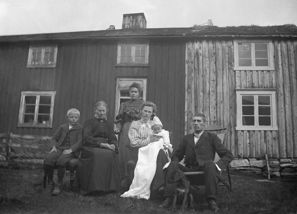 Leirfjord. Familie med dåpsbarn i lang dåpskjole foran huset.