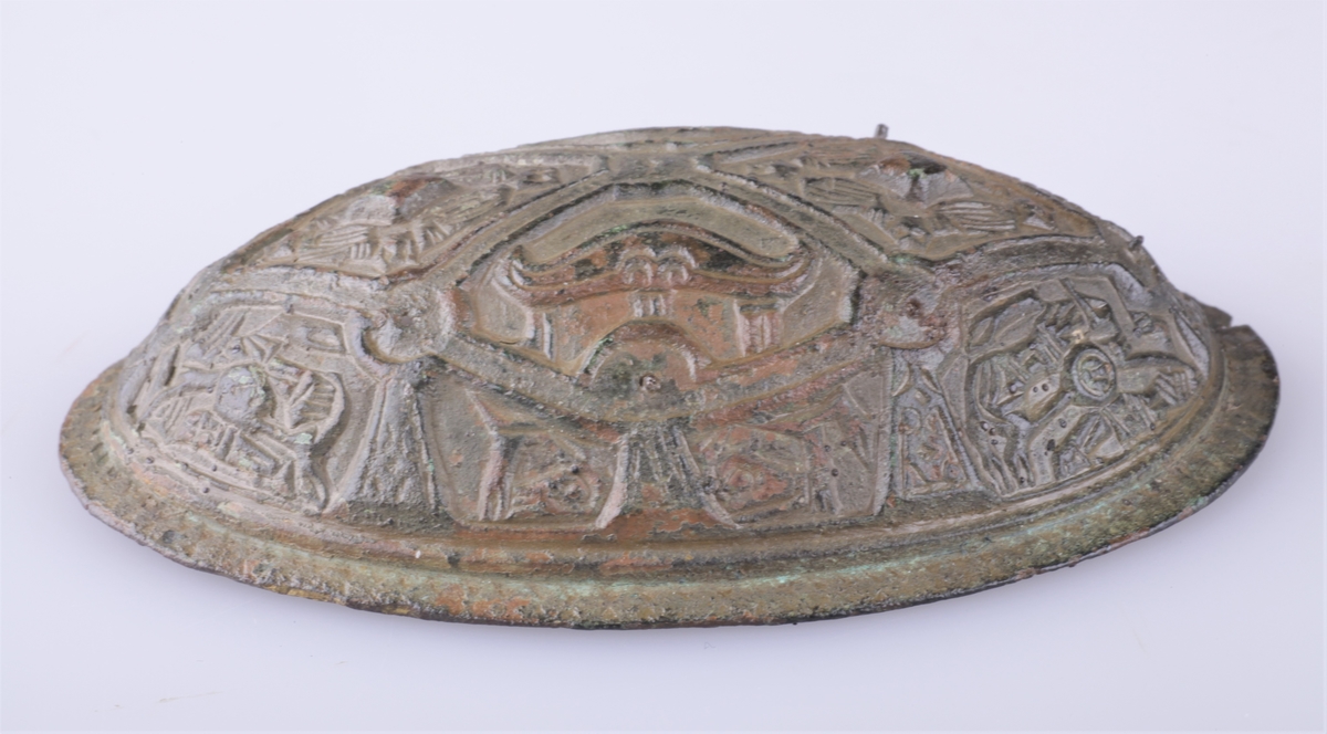 Oval bronsespenne med støpte ornamenter fra vikingtid. Variant av type Rygh 647. Funnet i en haug på gården Tråset i Fåberg i 1887.