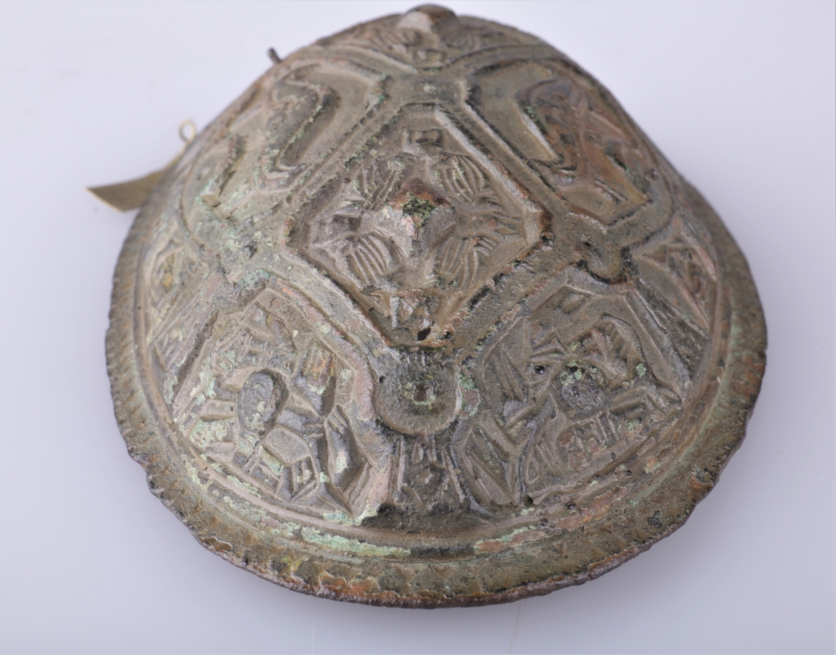 Oval bronsespenne med støpte ornamenter fra vikingtid. Variant av type Rygh 647. Funnet i en haug på gården Tråset i Fåberg i 1887.