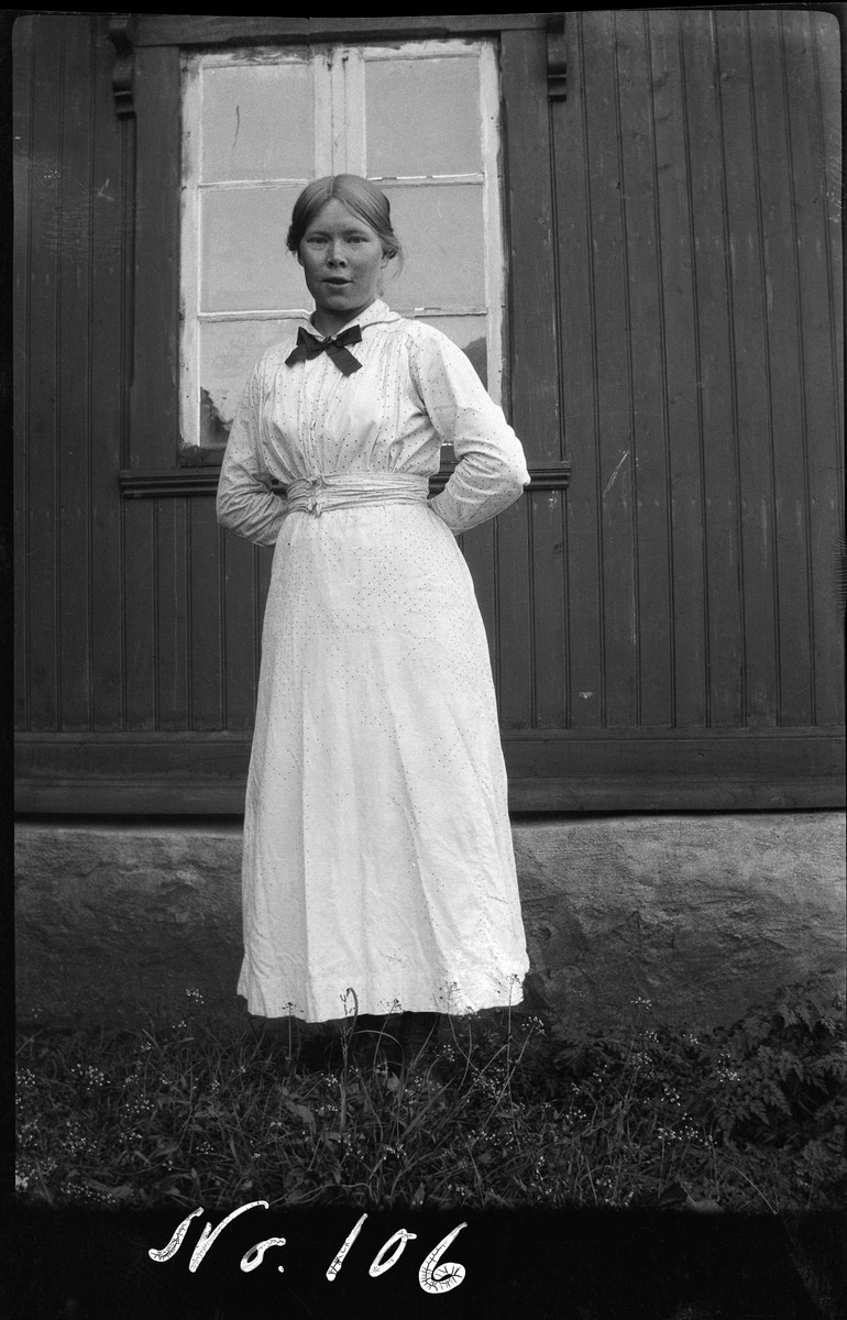 Portrett av en ung kvinne, fotografert stående utendørs foran en husvegg.