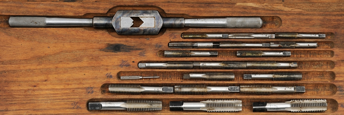 Gjengevertøy i original trekasse fra produsenten Greenfield tap and Die Corporation, USA bestående av seks (runde) gjengebakker/-snitt, 19 gjengetapper, ett svingjern for gjengetapper og ett svingjern for gjengebakker. Tappene øverst i eget brett. Skrinet og verktøyet bærer preg av å ha blitt brukt, men er i god stand.