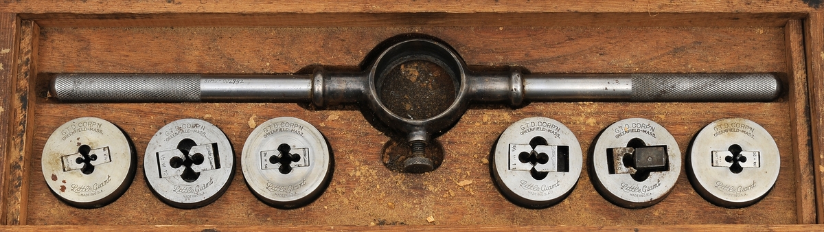 Gjengevertøy i original trekasse fra produsenten Greenfield tap and Die Corporation, USA bestående av seks (runde) gjengebakker/-snitt, 19 gjengetapper, ett svingjern for gjengetapper og ett svingjern for gjengebakker. Tappene øverst i eget brett. Skrinet og verktøyet bærer preg av å ha blitt brukt, men er i god stand.