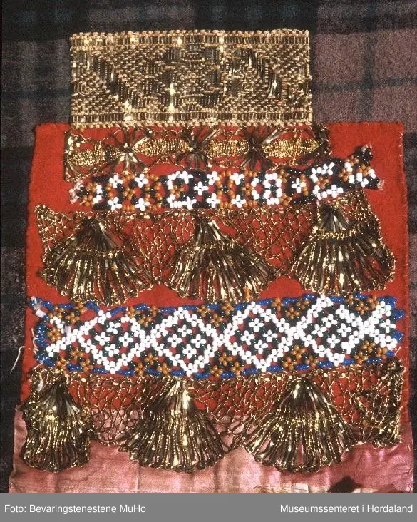 Bringeduk sett saman av ulike border. Øvst er montert ein rosa silkekvarde, under kjem ein kronekvare i gull, ei bord av perlenett, ein kronekvarde, ei smal bord av perlenett og ein smal kronekvarde, alt montert på raudt klede. Nedst, nedanfor kledet, ein liten bit av eit gullfarga metallband. Det raude kledet er montert på eit breiare, rutete ullstoff. Bakstykke av eit blått bomullsstoff.