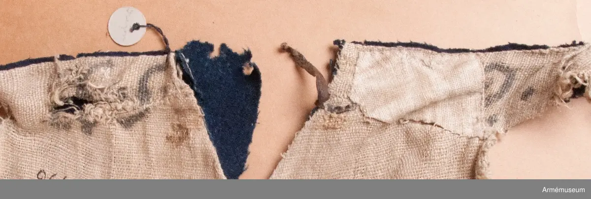 Blå ridbyxor med gula revärer och skinnskodda ben och byxbak.

Byxorna är sydda av ett ganska tunt blått kommisskläde, och är helfodrade med oblekt linne- eller hampalärft.
Modellen är konstruerad med två fram- och två bakstycken, och har hel lucka fram som har knäppts mot en gördel eller linning. Luckan har 5 knapphål fram, varav tre har knäppts mot gördeln. I luckans sidor upptill sitter två spänntampar för knäppning bak i ryggslutet. I sömmen bak sitter en infälld kil för reglering av midjevidden, samt en hank av läder för upphängning.
I sidan har byxorna revärar av 4 cm breda gula redgarnsband.
Byxbenen är skodda med brunt skinn i en höjd av ca 36 cm nertill. Kanten är formad i två bågar fram och en spets bak. Skinnskoningen fortsätter på baksidan upp på insidan av låren och i byxbaken.
Byxorna är mycket trasiga och malätna, och både yttertyg och foder har lagats ett flertal gånger under deras användningstid.
Samtliga knappar saknas förutom i höger byxben längst ner där det sitter rester av enkla skinnknappar i varje sida.

Märkt på insidan "LS No 2".