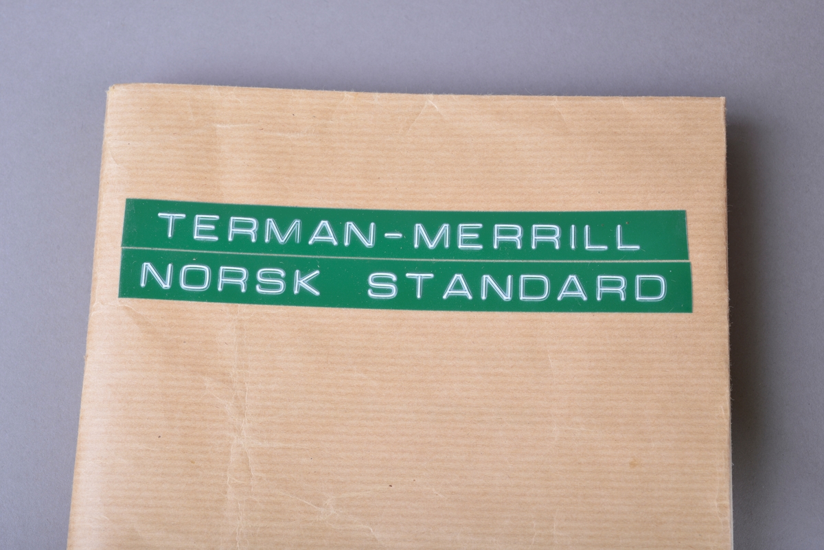 Rektangulær brun koffert av papp, med håndtak og lås. Inne i kofferten er det små pappesker. Pappeskene inneholder små treklosser, plater med pålimte miniatyr-leker. Blant annet dukke, hund seng, saks, pipe. I tillegg er det flere små knapper, notatblokk og tekstilbånd. I kofferten ligger også en bok merket "TERMAN-MERRILL // NORSK STANDARD".