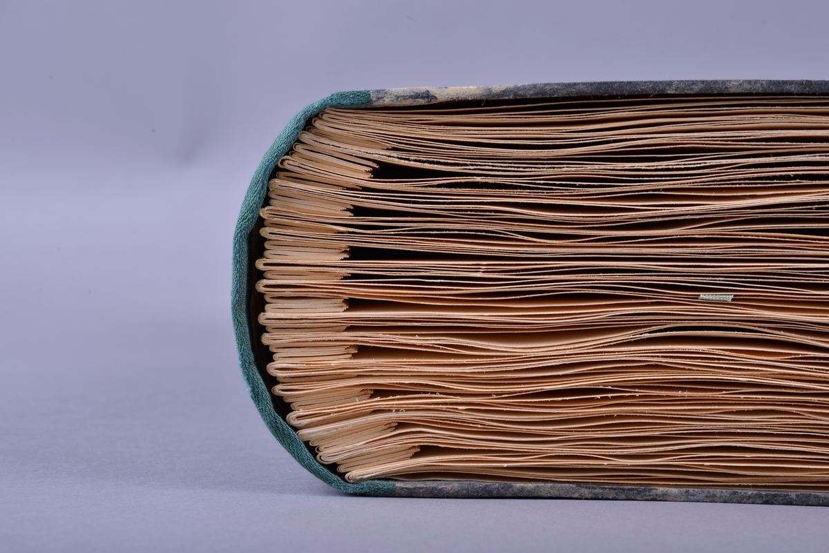 Innbundet bok med punktskrift. Tosidig trykk. Gråsvart omslag av kartong. Forsats av gult papir. Sidene er av gult papir. Tekstilhalvbind; ryggen og hjørnene er forsterket med grønn tekstil.