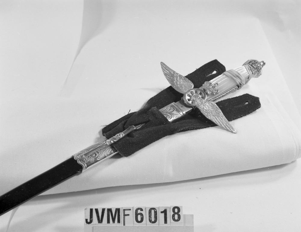 Paradvärja tillverkad av G. E Svalling i Rosenfors utanför Eskilstuna. Värjan hade en enbart ceremoniell funktion, och är inte vässad. Handtaget pryds av pärlemorpaneler, och den vinghjulformade parerstången, svärdsknoppen och andra detaljer är förgyllda. Baljan är av fint läder och är uddklippt i kanten.

Parerstången är märkt C.A, A.D. EK