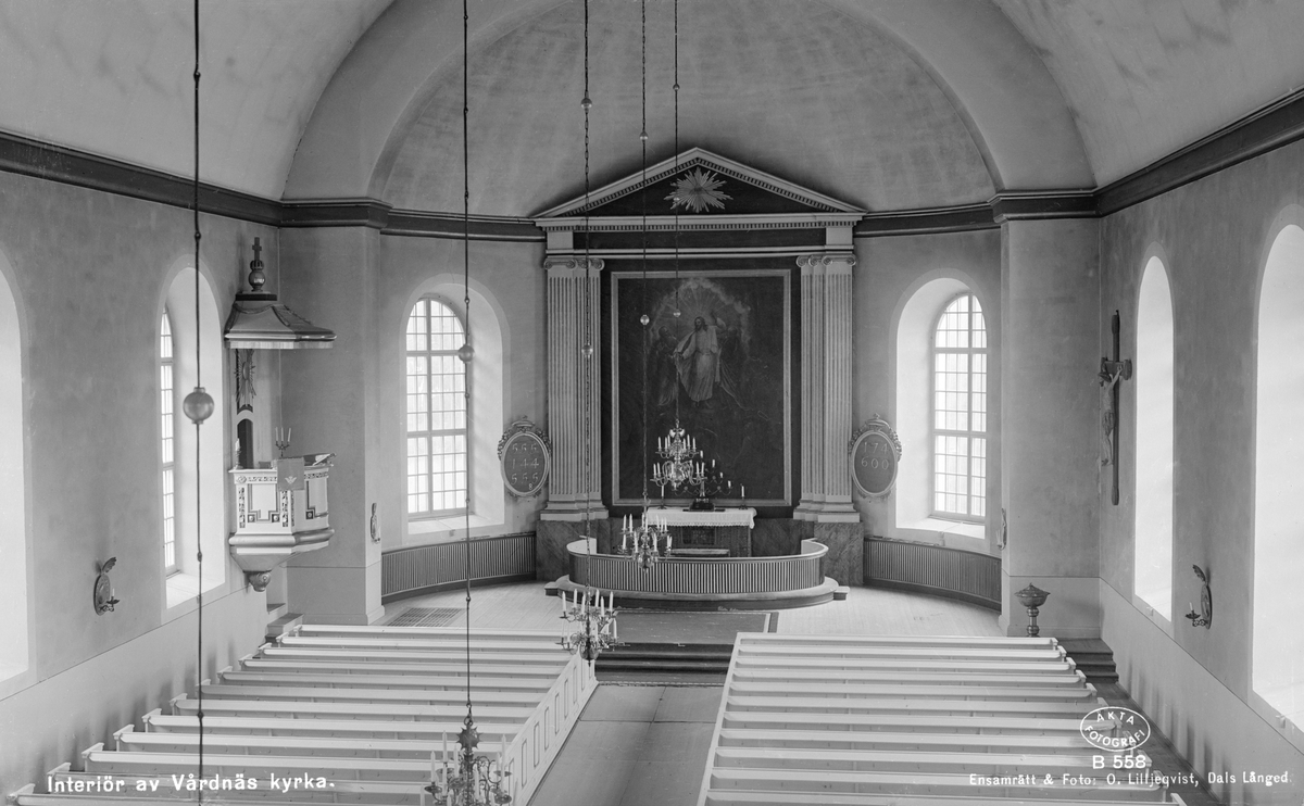 Interiör av Vårdnäs kyrka. Likt många äldre kyrkor bär den komplicerad byggnadshistoria. Nuvarande skapelse stod färdig 1796. Invändigt målades kyrkan av fabrikör Carl Fredrik Beurling i Norrköping. "Coleuren skall bliva pärlfärg med litet svart" heter det, och denna sengustavianska färgställning är delvis bevarad. Beurling levererade också predikstolen, som skänktes av grevinnan Hedvig Eleonora Falkenberg, född Wachtmeister. Altartavlan är målad 1802 av den vid tiden mycket anlitade kyrkomålaren Pehr Hörberg, som återgivit ämnet "Jesu förklaring med Moses och Aron".