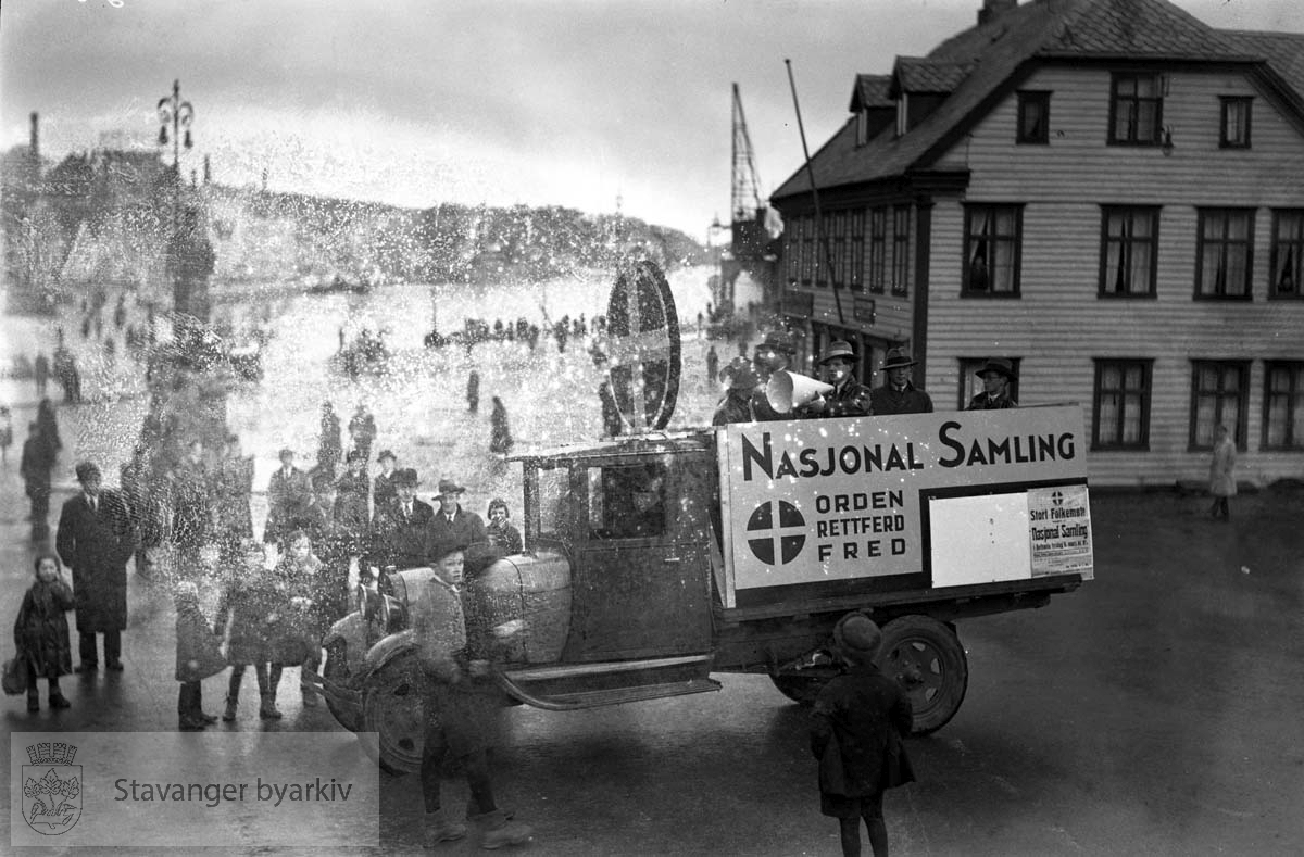 NS, Nasjonal Samling på torget mot vågen.Lastebil med velklingende, salgbare slagord..Bilen og folkene er der for å reklamere for et stort folkemøte (se plakat nederst til høyre på lasteplanet)