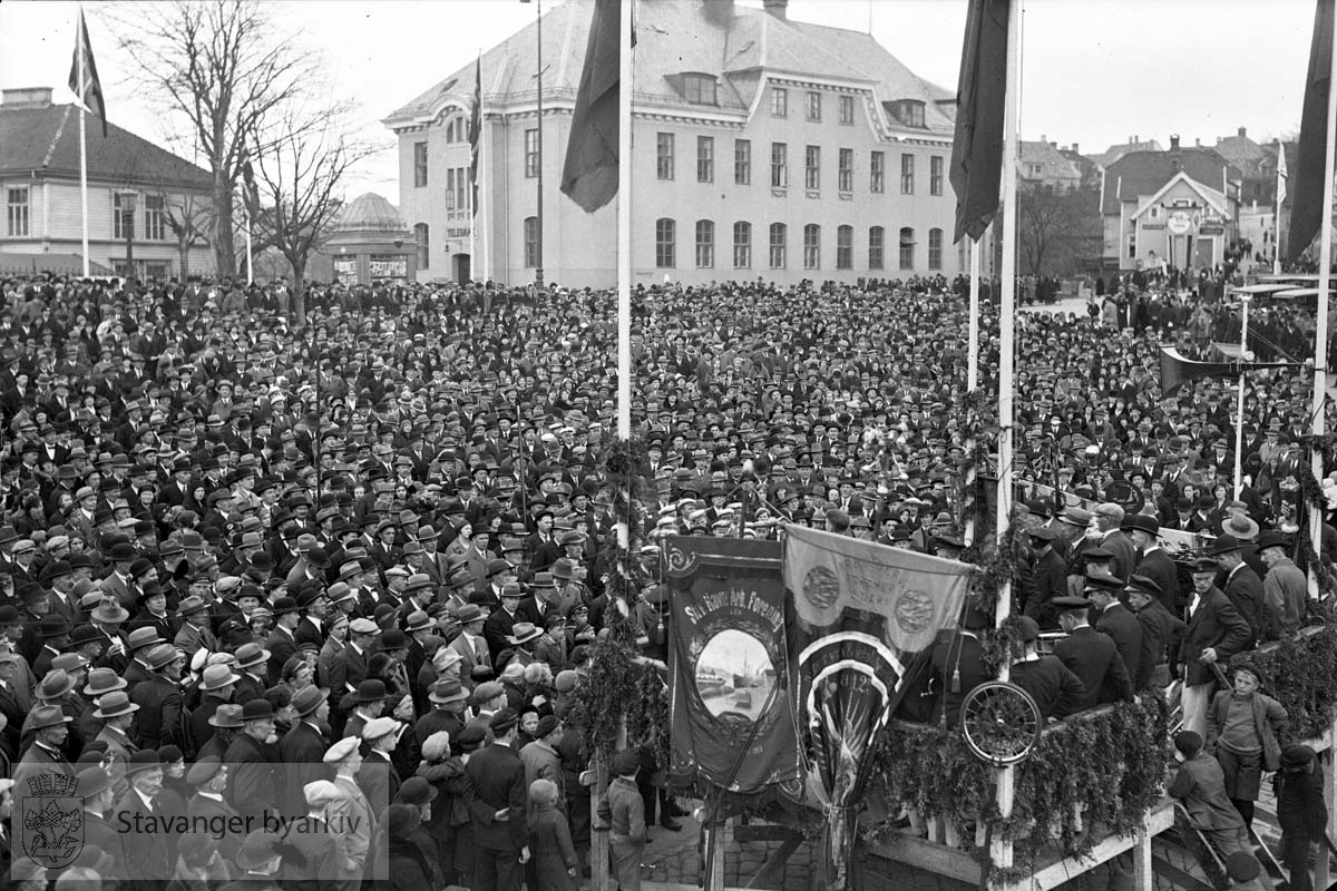 1. mai.folkesamling på torget..Posthuset i bakgrunnen.Podiet med faner nederst til høyre