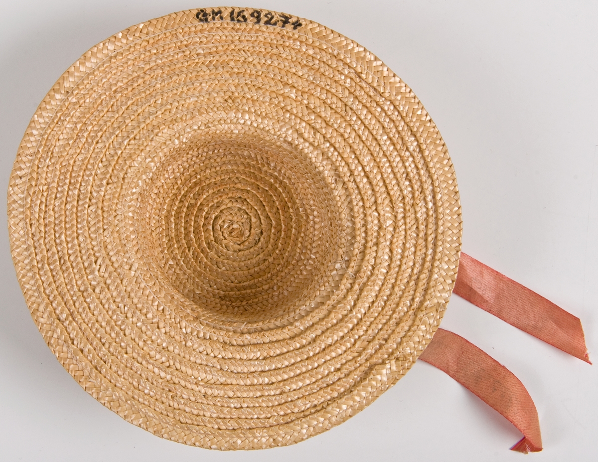Två dockhalmhattar med rött respektive blått band.
a) Med flätat kant och blått band med med guldtexten: "RÜGHEIMER & BECKER, 1897, Minne af Stockholms utställning." Diam 14,5cm.
b) Med rött band och svart text: som a. Diam 14,5.