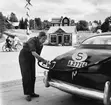 En kvinna tankar en Hudson Pacemaker årsmodell 1950. I bakgrunden två cyklister som står och samtalar. Bilden tagen i Dalarna år 1952.