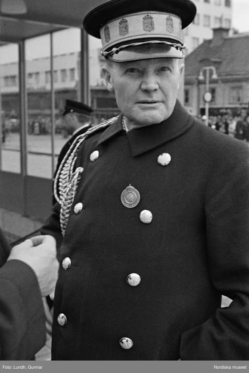 Invigning av Södra Bantorgets (Medborgarplatsen) tunnelbanestation på Södertunneln den 30 september år 1933, Kung Gustaf V kliver in i en bil, porträtt av en man i uniform - en chaufför vid Kungliga Hovstallet, detalj av en bil med lykta och skärm, en grupp män går ut ur en tunnelbanenedgång på Södra Bantorget - män i uniform gör honnör och i bakgrunden står människor i öppna fönster.