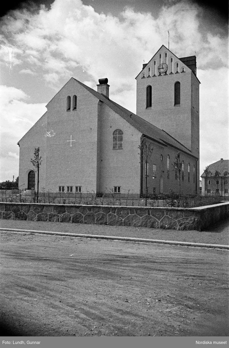 Exteriör av Höganäs kyrka, Himmelfärdskyrkan, under byggnation och som nybyggd, en kyrkobyggnad omgiven av byggnadsställningar, två bilar parkerade framför en kyrka.