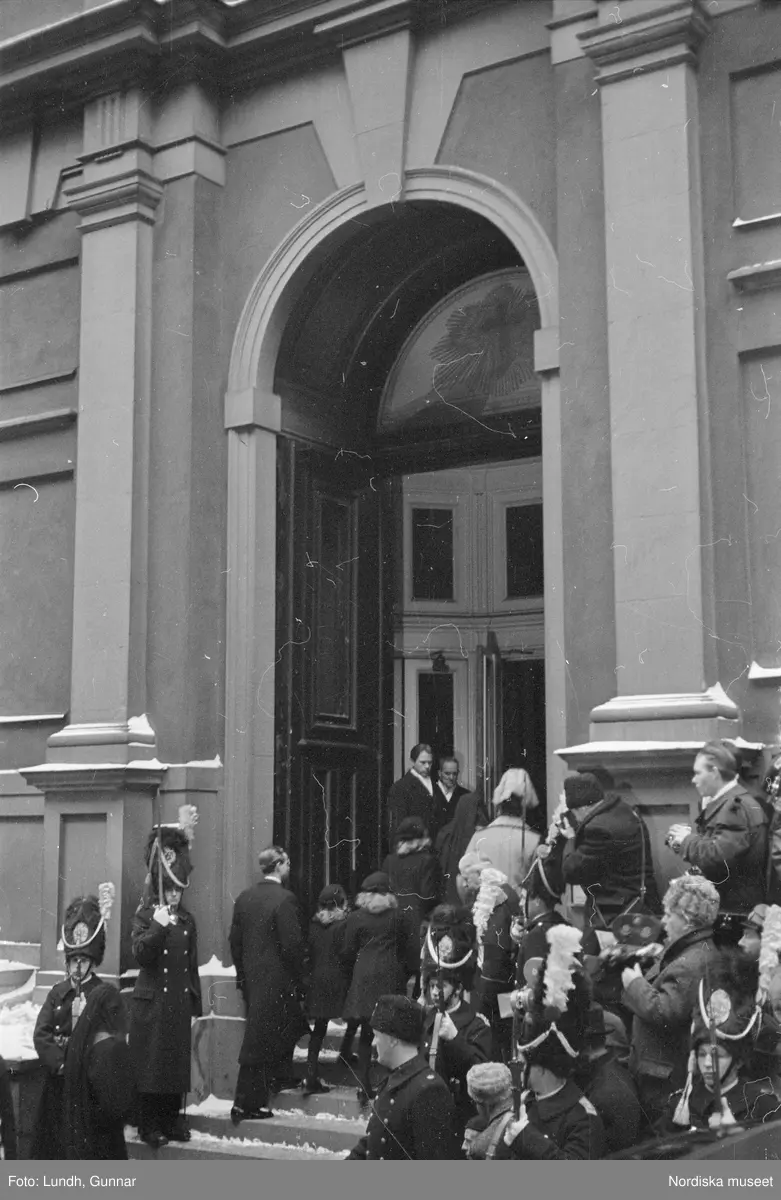 Troligen begravningen av Prins Gustaf Adolf, en kista bärs ut från Storkyrkan, kungafamiljen går ut från Storkyrkan, militärer i uniform står i givakt, kistan står på en katafalk som dras av hästar, en folksamling står längs vägen när begravningsföljet passerar.